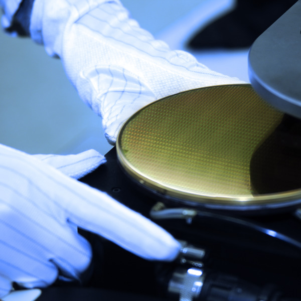 hands wearing gloves working with a golden, round silicon wafer hands wearing gloves working with a golden, round silicon wafer
